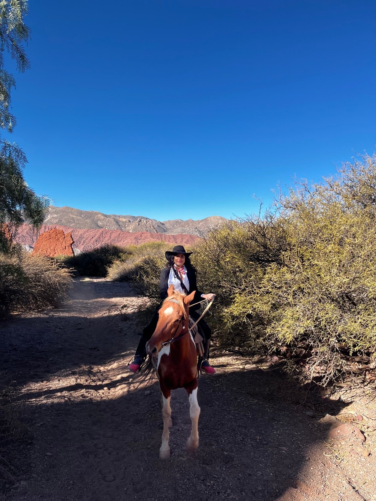 Dana recorre a caballo un sendero entre la vegetación y las montañas de Tupiza
