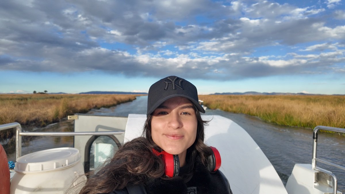Mujer en la cubierta de una embarcación en un canal entre totorales del lago Titicaca